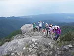 6人ほどのグループが愛子岳で眼下の景色をバックにポーズを取っている写真