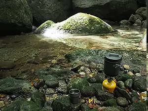 河原で登山用のバーナーを使ってお湯を沸かしている写真