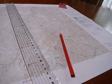 25000分の1地形図の上に長い定規と赤鉛筆が広がっている写真
