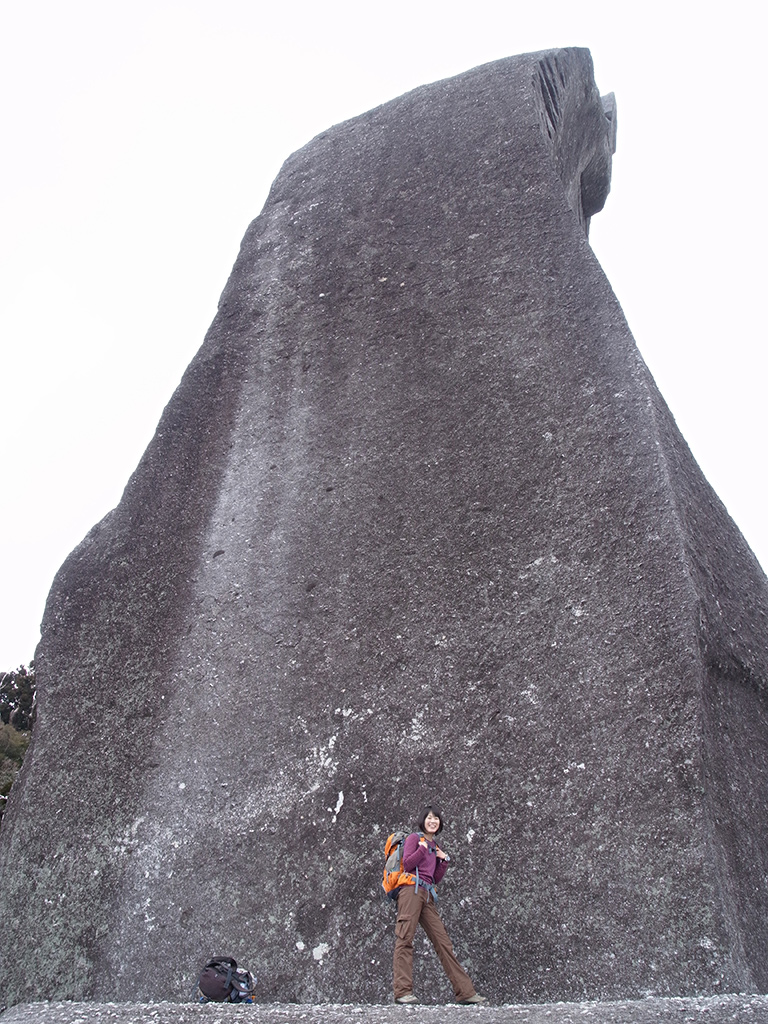 太忠岳山頂に鎮座する巨岩・天忠石の前でポーズを取る参加者Tさんの写真