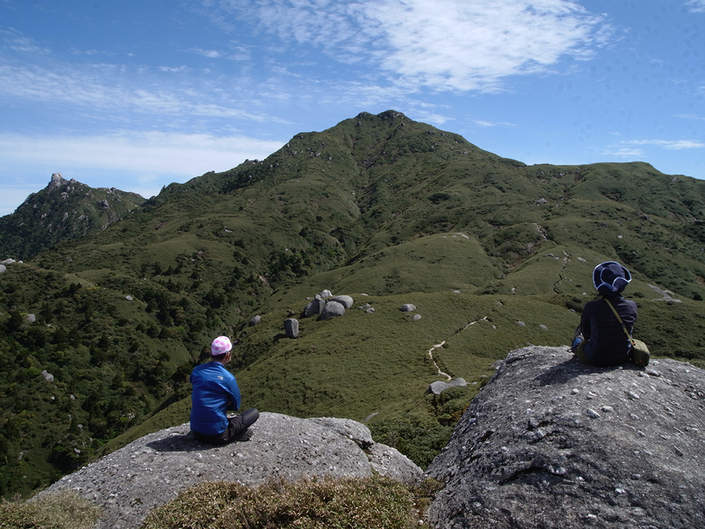 平石岩屋の巨石群に乗り、ついさっきまで居た宮之浦岳を座って眺める二人の写真