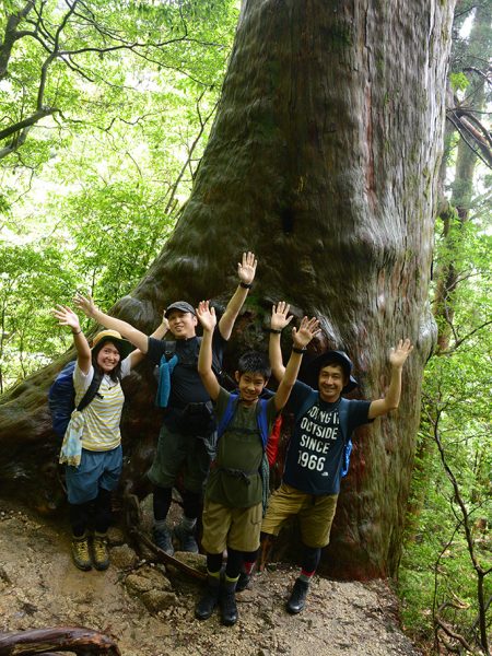 子宝杉と呼ばれる杉の前で、4人が両手を広げてポーズを取っている写真