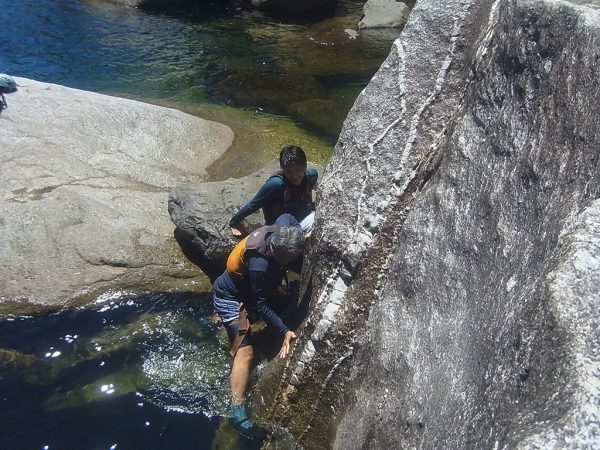 岩を登る足がかりが恐ろしく小さく滑るので、攻略方法を話しながら登るお父さんを応援する息子の写真