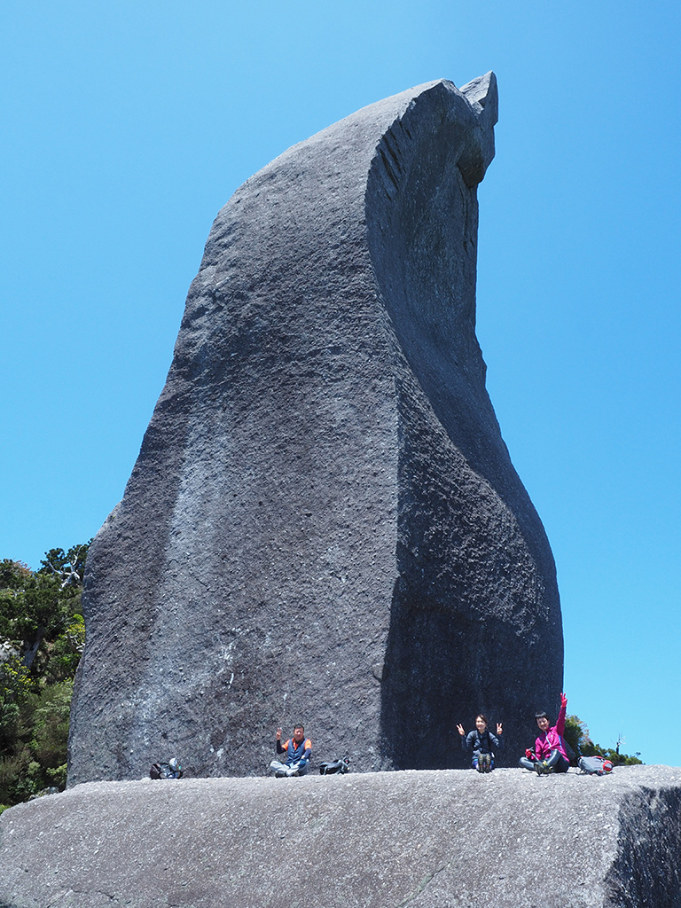 山頂に鎮座する巨岩・天忠石の前で参加者3人が大きく手を広げてポーズをとっている写真