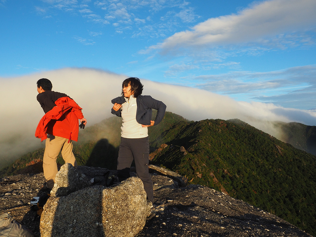 山頂の風に煽られながらジャケットを着る二人の写真と、山頂からの景色