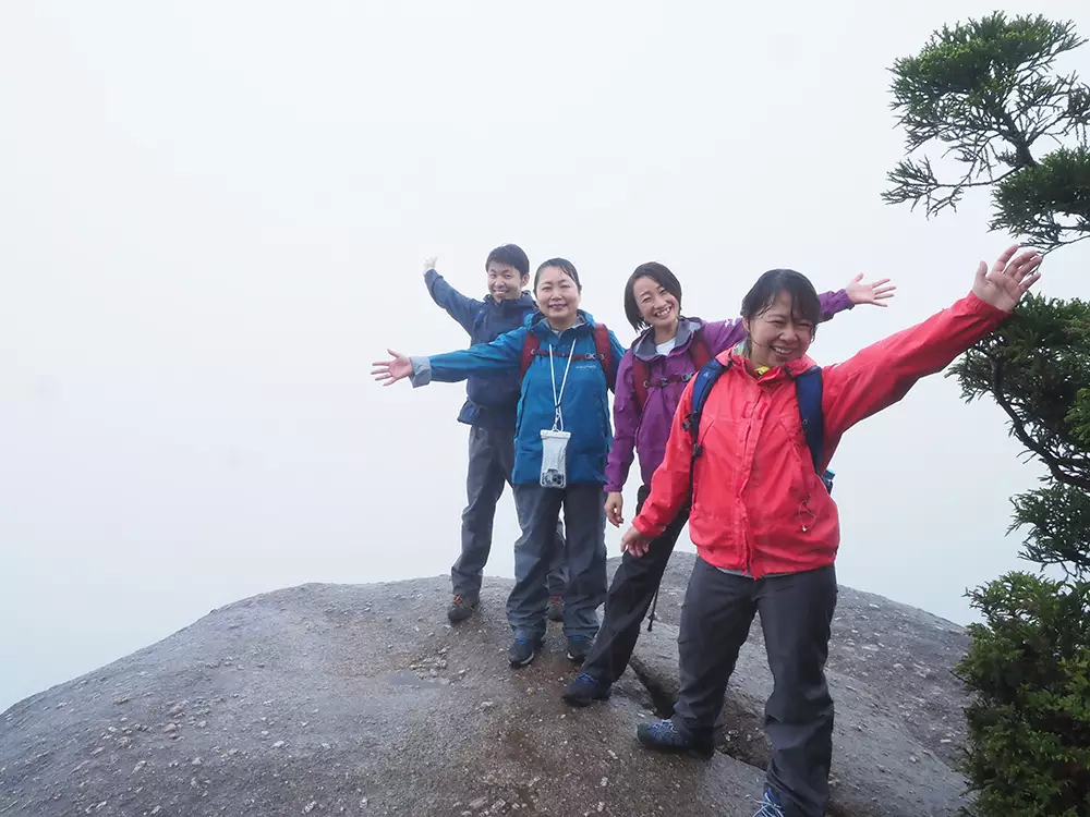 雲に覆われて真っ白な太鼓岩の上でポーズを撮る4人の写真