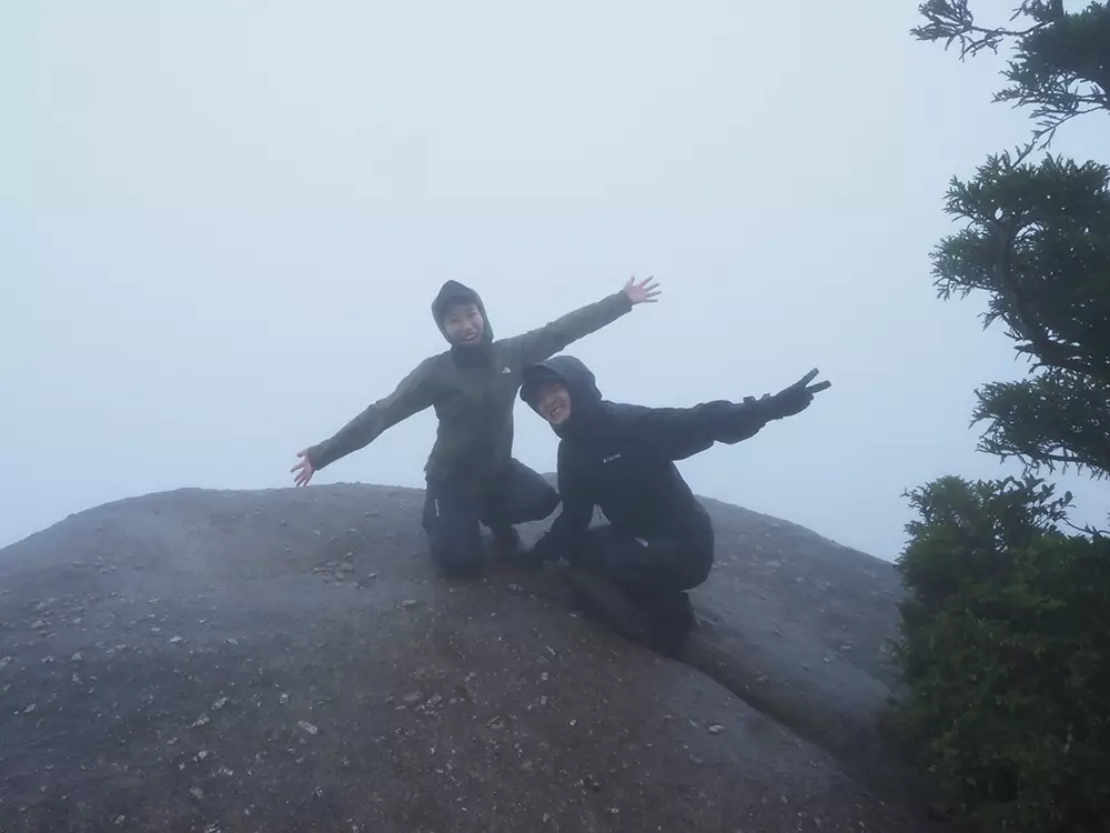 雲と小雨で真っ白な太鼓岩の上で両手を広げる二人の写真