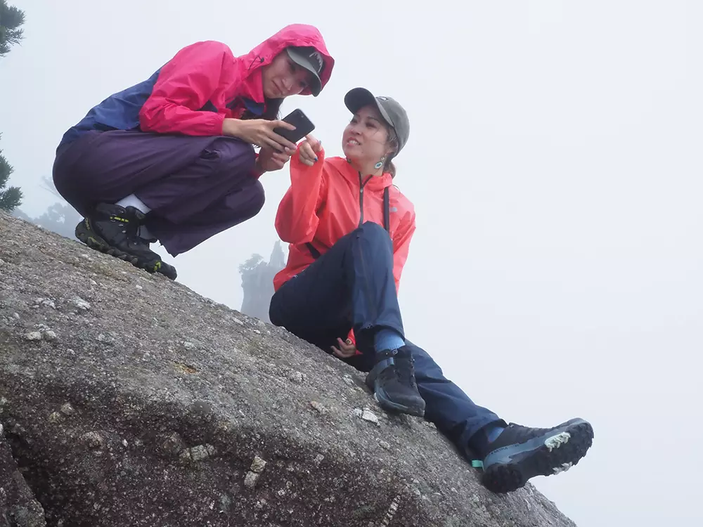 雲に包まれた太鼓岩の上で楽しそうに話をする二人の写真